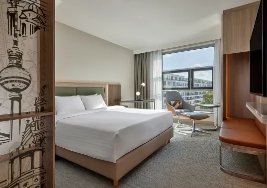 Modernes Hotelzimmer mit Doppelbett, Schreibtisch, Stuhl und großem Fenster mit Stadtblick.