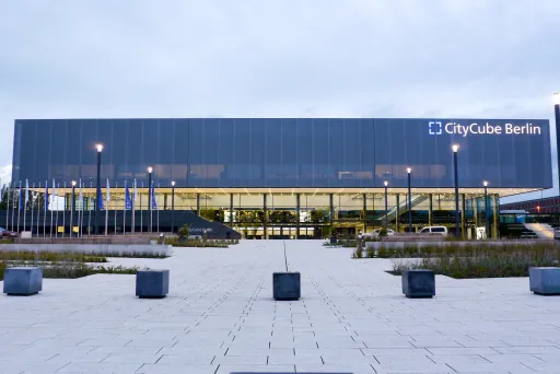 Moderne Glasfassade des CityCube Berlin bei Dämmerung, beleuchtet und umgeben von Parkplatz.