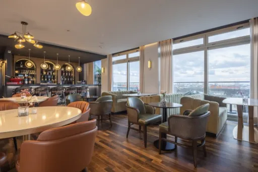 Modernes Café mit großen Fenstern, gemütlichen Sitzmöbeln und Barbereich bei Tageslicht.