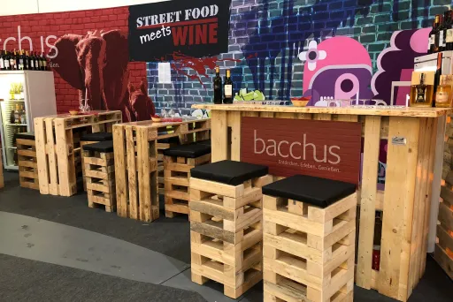 Barbereich aus Holzpaletten mit schwarzer Sitzfläche, bunte Wand mit Street-Food-Graffiti.