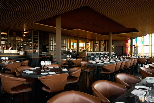 Modernes Restaurant mit braunen Ledersesseln und gedeckten Tischen, warm beleuchtet.