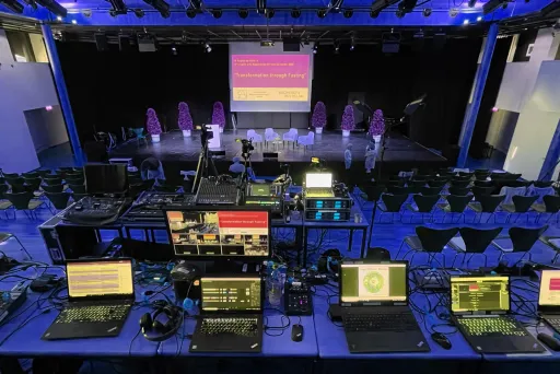 Regieraum mit Technik und Laptops vor einer leeren Bühne in einem Veranstaltungsraum