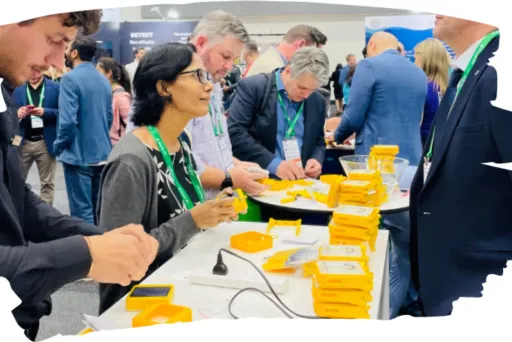 Menschen bei einer Messe, stehen an Tischen mit gelben Schachteln und Unterhaltungen.