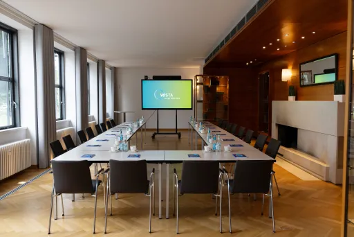 Moderner Konferenzraum mit großem Tisch, Stühlen und Bildschirm, Tageslicht durch Fenster