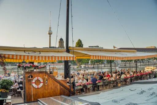 Sonnige Terrasse von Spree Fumée, Markisen spenden Schatten, zahlreiche Gäste genießen das Ambiente bei strahlendem Wetter.