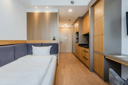 Modernes Einzelzimmer mit Holzboden, Bett, Schreibtisch und Fernseher an der Wand.