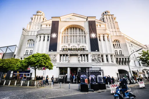 Historisches Gebäude bei Tageslicht, Menschen stehen davor, Bäume am Rand.