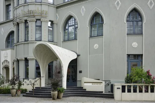 Hoteleingang mit modernem weißen Vordach, großen Fenstern und grauer Fassade