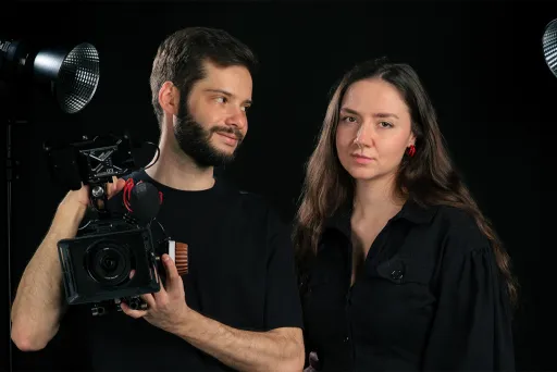 Zwei Personen im Fotostudio, einer hält eine Kamera, beide tragen schwarze Kleidung.