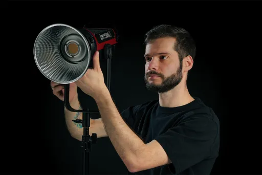 Mann stellt Studiolicht mit Reflektor vor schwarzem Hintergrund ein.