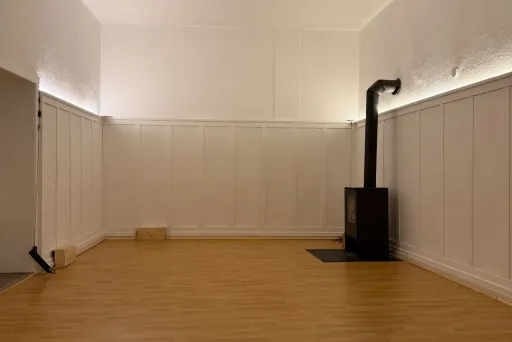 Leerer Raum mit hellem Holzfußboden und einem schwarzen Ofen in der Ecke