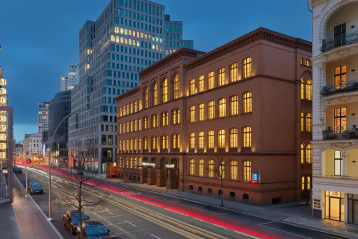 Abendliche Stadtstraße mit beleuchteten Bürogebäuden und Lichtstreifen vorbeifahrender Autos.