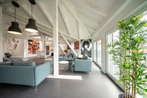Modernes Loft mit blauen Sofas, großen Fenstern, Kunstwerken und einer grünen Pflanze.