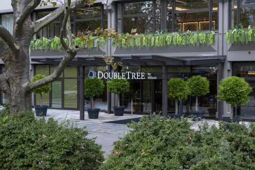 Hoteleingang von DoubleTree mit Glasfassade und grünen Pflanzen in Töpfen.