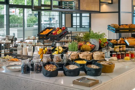 Frühstücksbuffet mit frischem Obst, Brot, Müsli, Marmelade und Säften in modernem Restaurant.