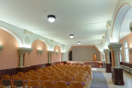 Leerer Saal mit Holzstühlen, gewölbten Decken und hellem Licht.