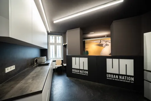 Moderne Küche mit schwarzer Theke und weißen Schränken, Urban Nation Logo sichtbar