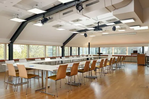 Moderner Konferenzraum mit langen Tischen, Holzstühlen und großen Fenstern