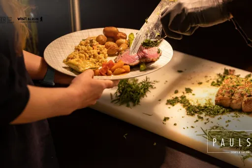 Eine Person erhält auf einem Teller Fleisch und Beilagen an einer Buffetausgabe.