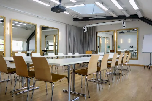 Moderner Konferenzraum mit langen Tischen, Holzstühlen und großen Spiegeln an den Wänden.