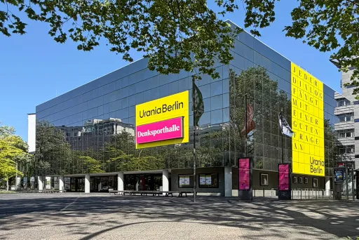 Urania mit Humboldt Saal in Berlin mit gelben und pinken Bannern, umgeben von Bäumen.