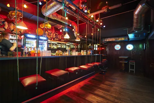 Leere Bar mit roten Hockern, bunter Beleuchtung und Zapfhähnen am Tresen.