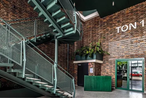 Modernes Foyer mit Backsteinwänden, grünem Tresen und Metalltreppe, Schild „TON 1“.