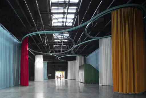 Großer Raum mit bunten Vorhängen und sichtbaren Stahlrohren unter der Decke.