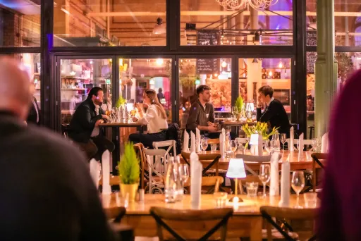 Menschen sitzen in einem gemütlichen, hell erleuchteten Restaurant und unterhalten sich.