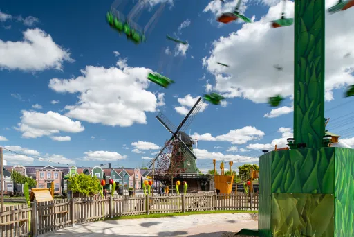 Windmühle im Freizeitpark bei sonnigem Wetter, Karussell im Vordergrund.