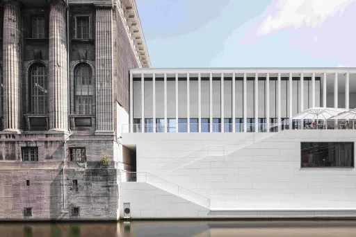 Altes Steingebäude neben modernem weißen Bau am Wasser.
