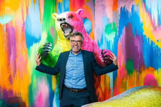 Mann vor farbigem Bärenkunstwerk, beide mit erhobenen Armen und fröhlichem Gesicht.