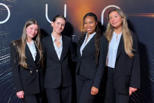 Vier lächelnde Messehostessen in eleganten schwarzen Business-Anzügen auf einem Corporate Event. Professionelles Promotion-Personalvon VPeople GmbH