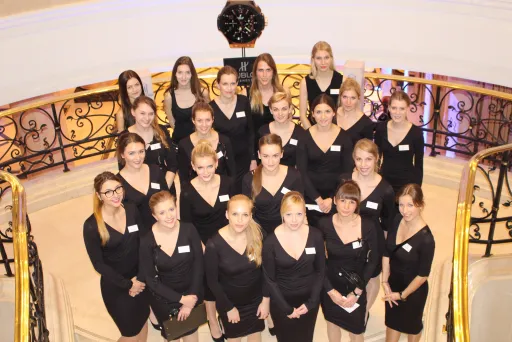 Gruppe junger Frauen in schwarzen Kleidern auf einer Treppe, alle schauen in die Kamera.