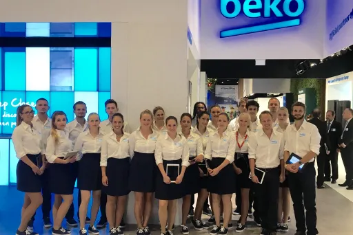Gruppe von Mitarbeitern in einheitlicher Kleidung vor einem beko-Stand auf einer Messe.