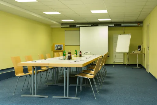 Konferenzraum mit langem Tisch, Stühlen, Leinwand und Flipchart.