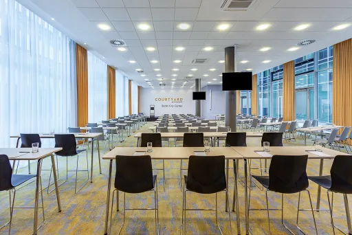 Moderner, heller Konferenzraum mit vielen leeren Tischen und Stühlen.