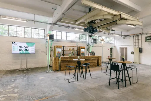 Heller, moderner Innenraum mit Bar, Stehtischen und Hockern in einer Industriehalle.