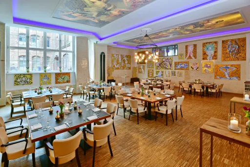 Helles Restaurant mit modernen Tischen, Stühlen und vielen Kunstwerken an den Wänden.