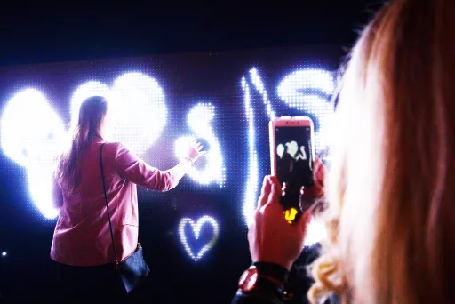Frau malt mit Licht auf dunkler Wand, eine andere Person fotografiert es.