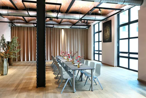 Großer, heller Raum mit langem gedecktem Tisch und modernen Stühlen, Holzfußboden, loftartig.