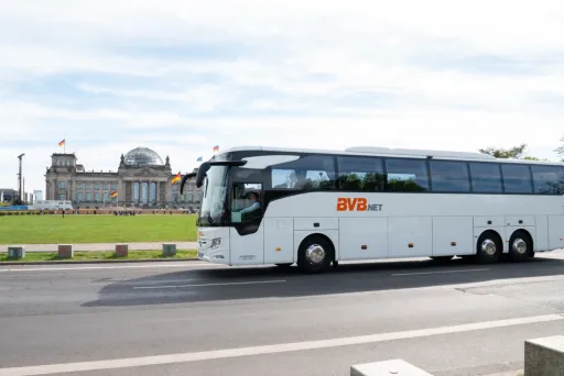 Ein BVB.net Reisebus fährt im Vordergrund auf der Straße, im Hintergrund der Reichstag in Berlin.