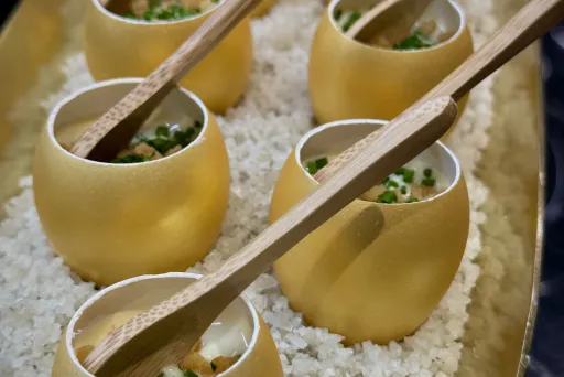 Kleine goldene Schalen mit Löffeln, serviert auf Reis, gefüllt mit Speise und Kräutern.