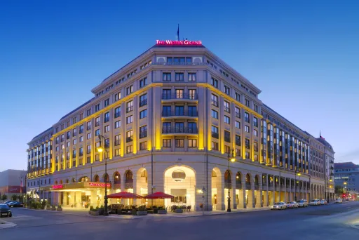 Großes, beleuchtetes Hotelgebäude an einer Straßenkreuzung bei Abenddämmerung.