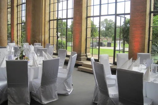 Elegant banquet tables with white chairs set by large windows overlooking a garden.