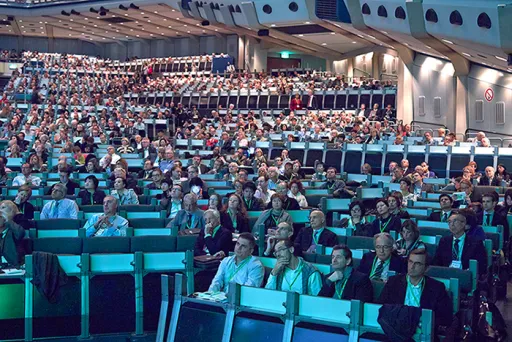 Großer Konferenzsaal mit vielen sitzenden, aufmerksam lauschenden Menschen.