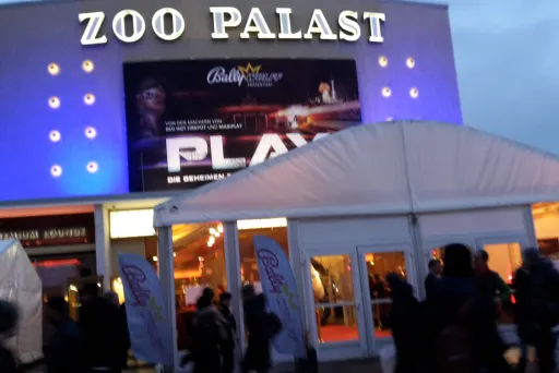 Kinoeingang Zoo Palast mit beleuchtetem Werbeplakat und wartenden Menschen.