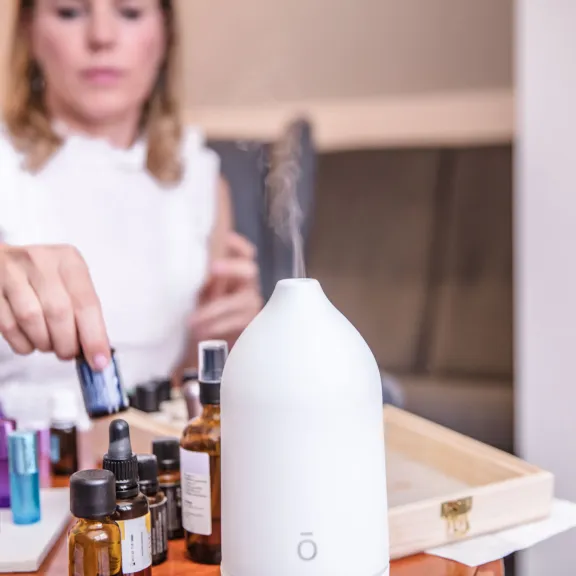 Frau legt ätherisches Öl neben einen Aromadiffusor auf einen Tisch.