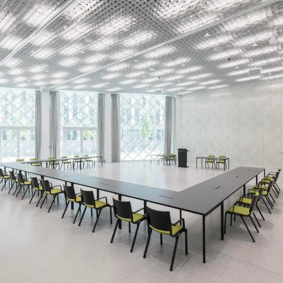 Großer heller Konferenzraum mit U-förmigem Tisch und vielen Stühlen.