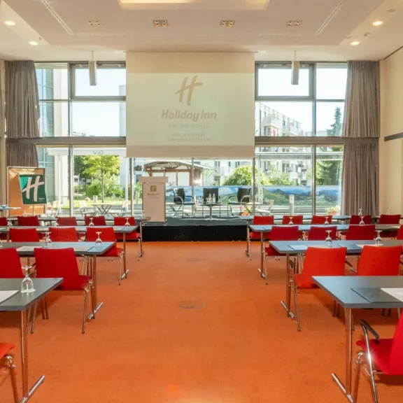 Heller Konferenzraum mit roten Stühlen, Tischen und großer Fensterfront.